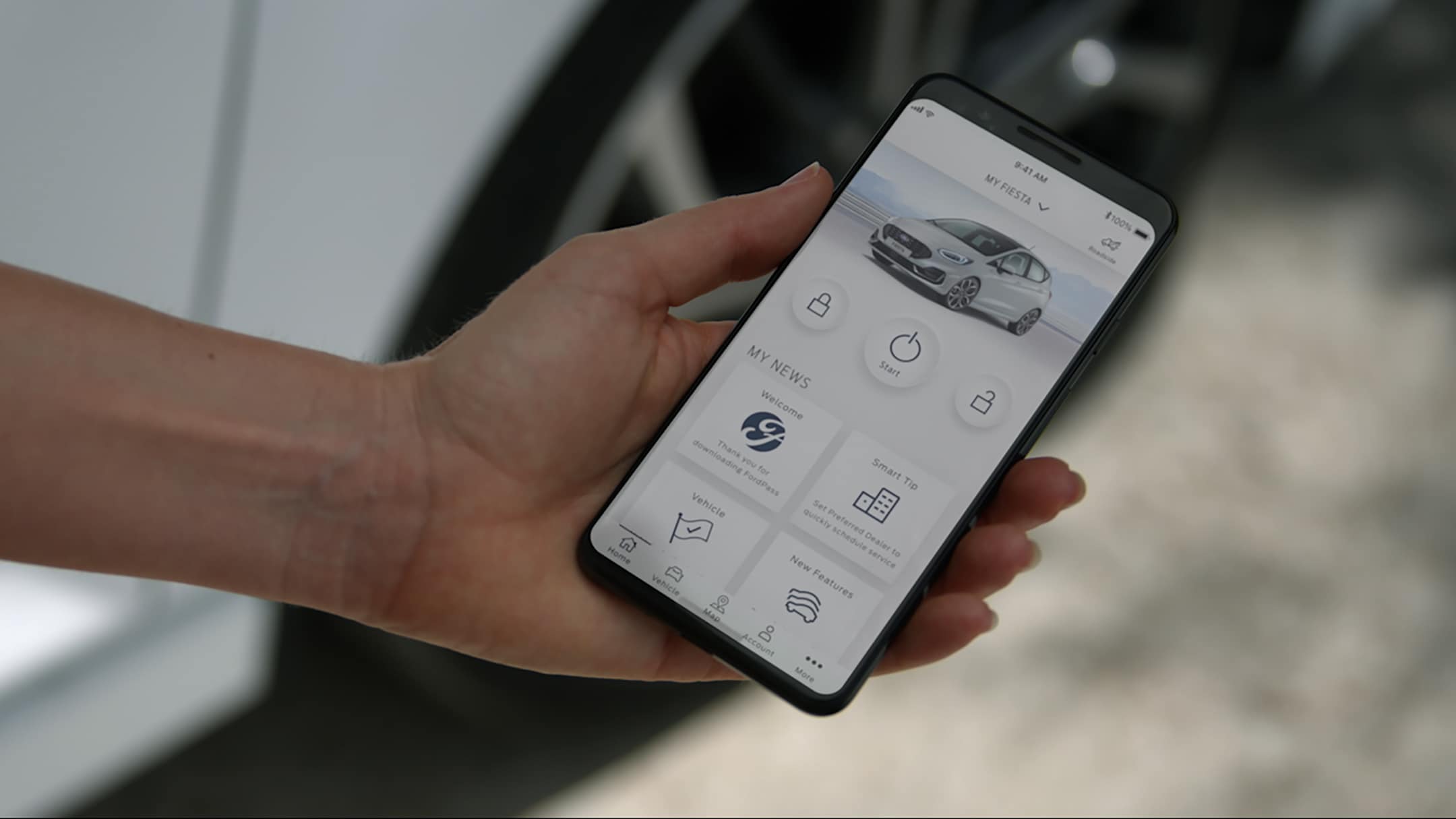 FordPass App auf einem Smartphone vor einem weissen Ford Fiesta ST.