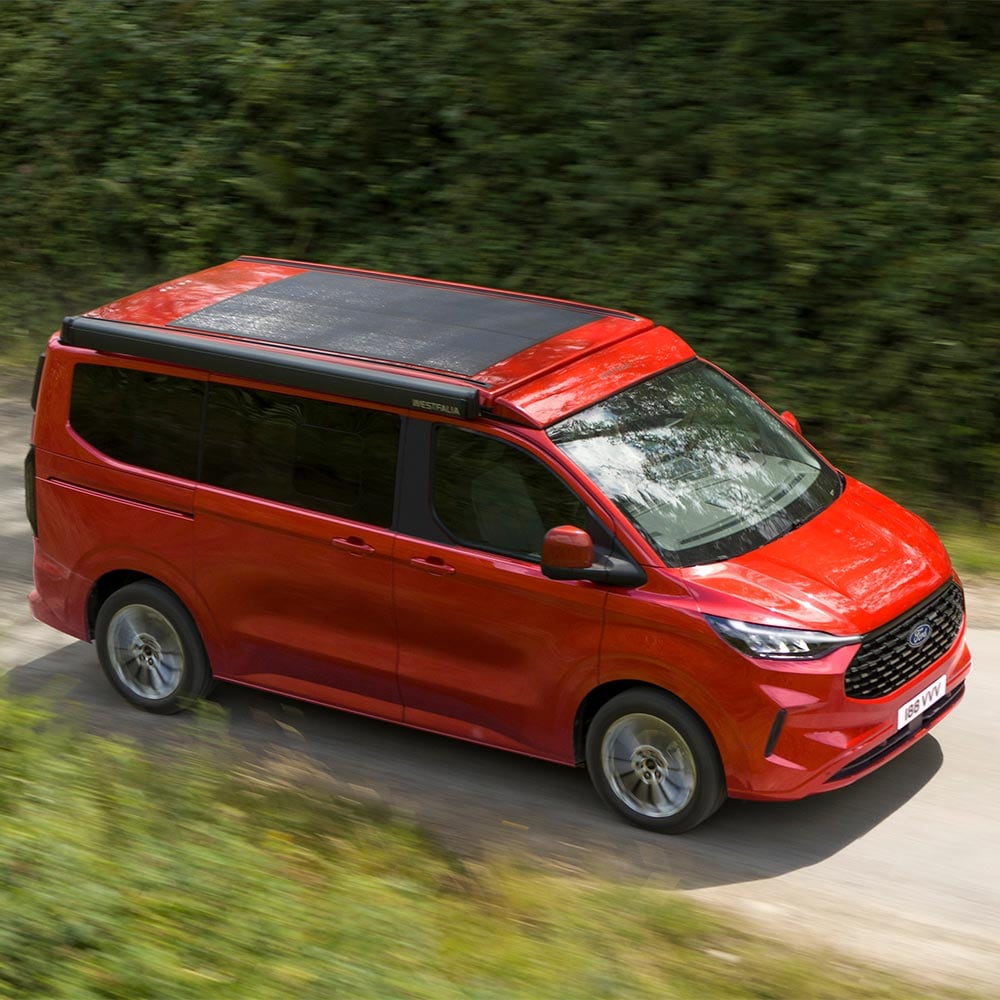 Roter Ford Nugget mit Solarpanel auf dem Dach fährt auf der Strasse. 