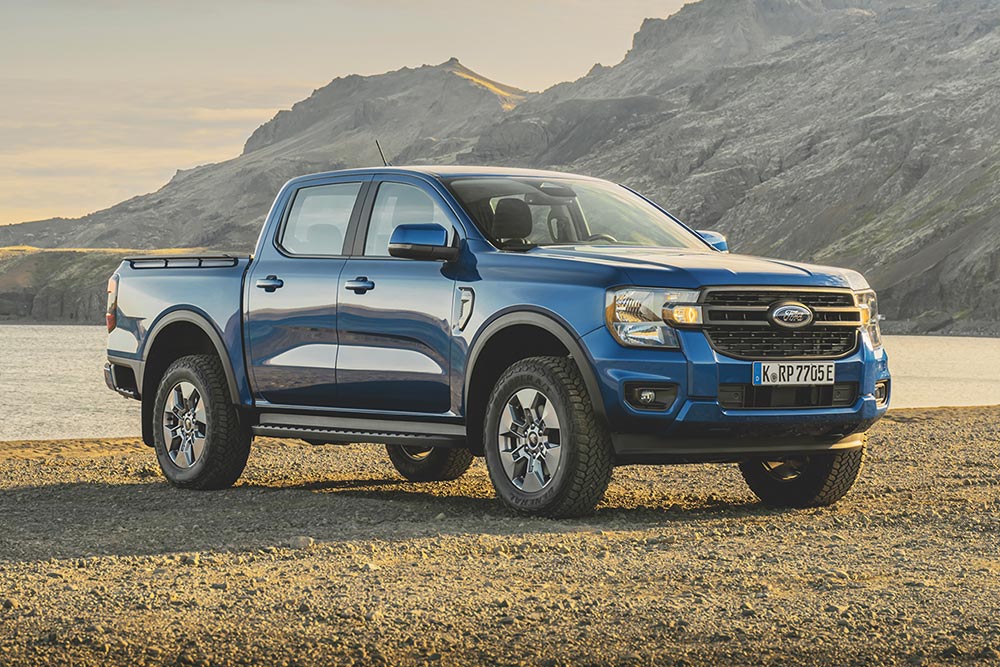 Blauer Ford Ranger am Ufer eines Sees, im Hintergrund schroffe Berge und dichte dunkle Wolken.