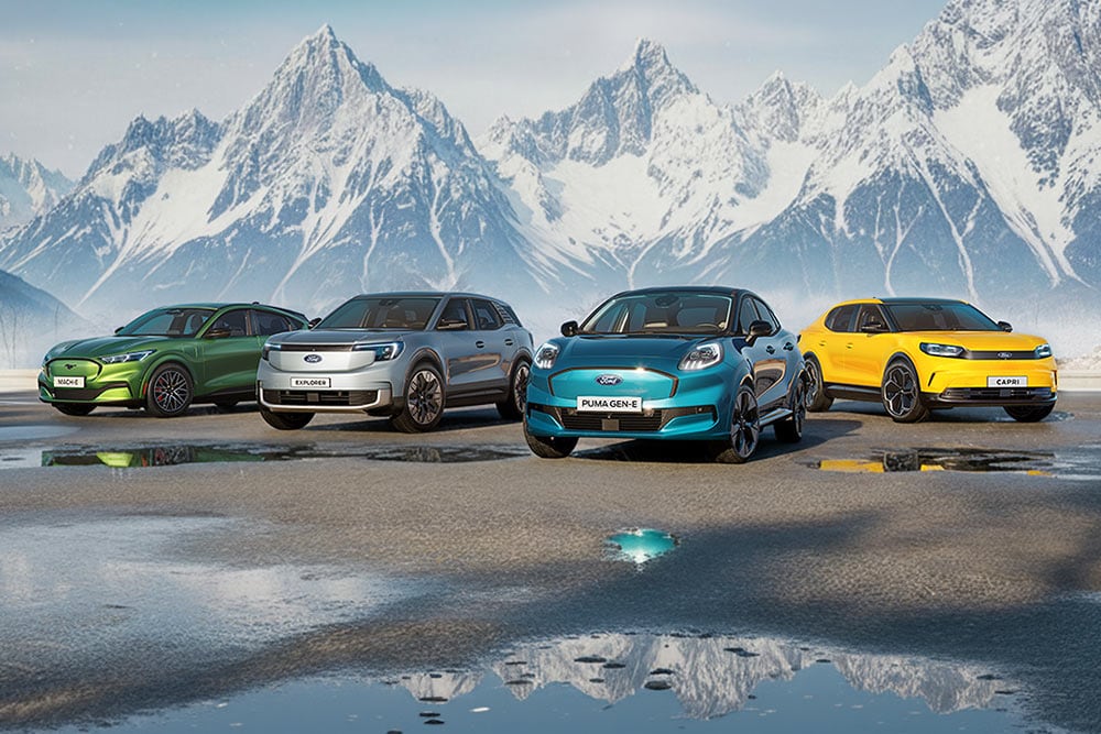 Vier bunte Ford-Modelle stehen nebeneinander auf nassem Boden vor einer verschneiten Gebirgskulisse.