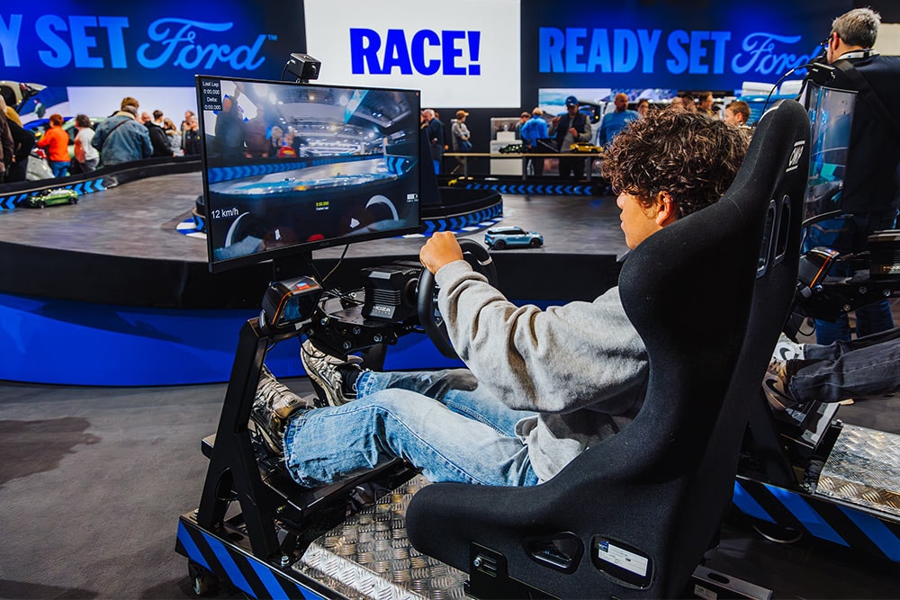 Ein Besucher spielt an einem virtuellen Rennsimulator auf einem modern beleuchteten Ford-Messestand