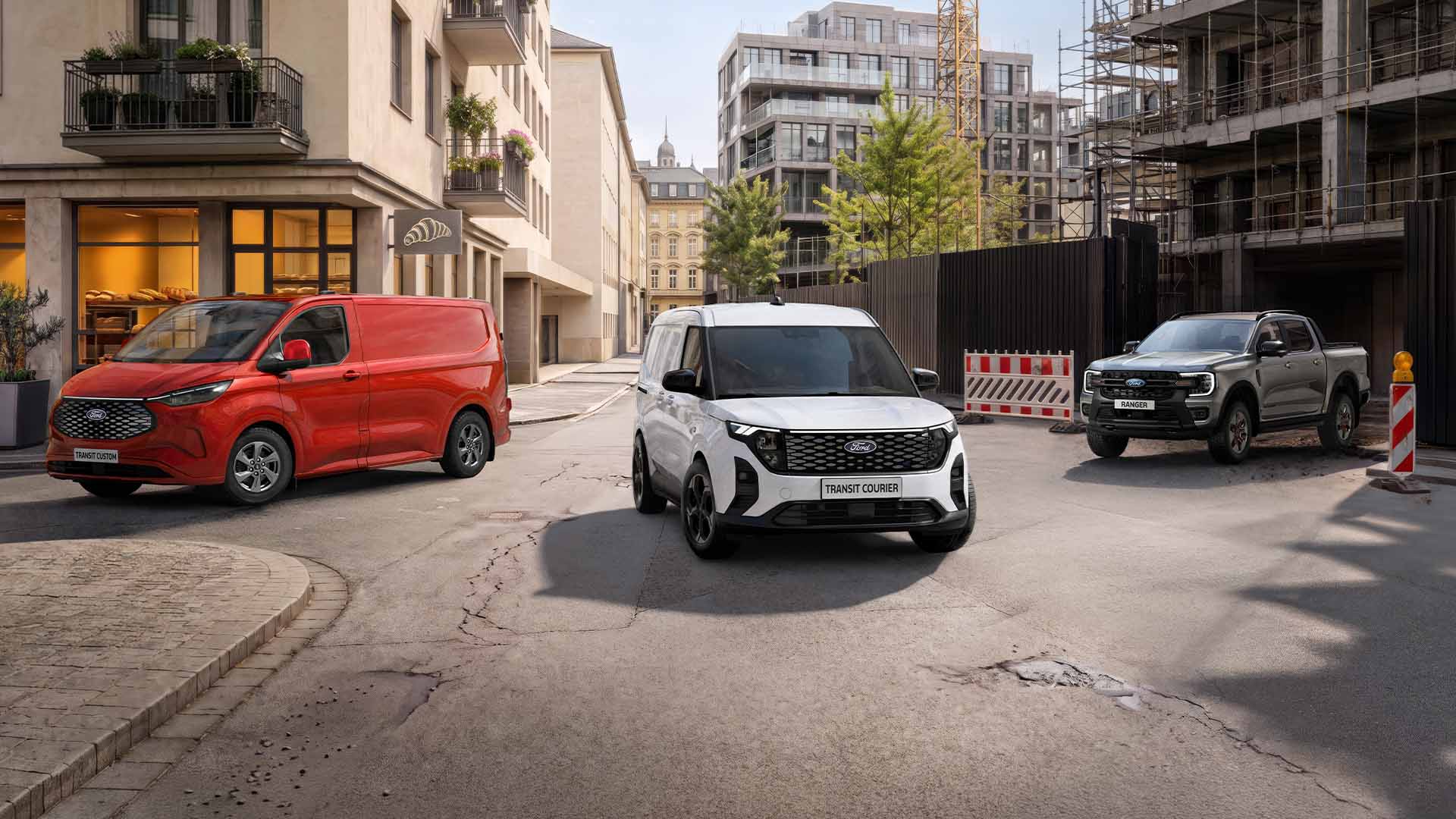Drei Ford-Fahrzeuge, ein roter Transit Custom, ein weißer E-Transit Custom und ein grauer Ranger, stehen auf einer Stadtstraße. 