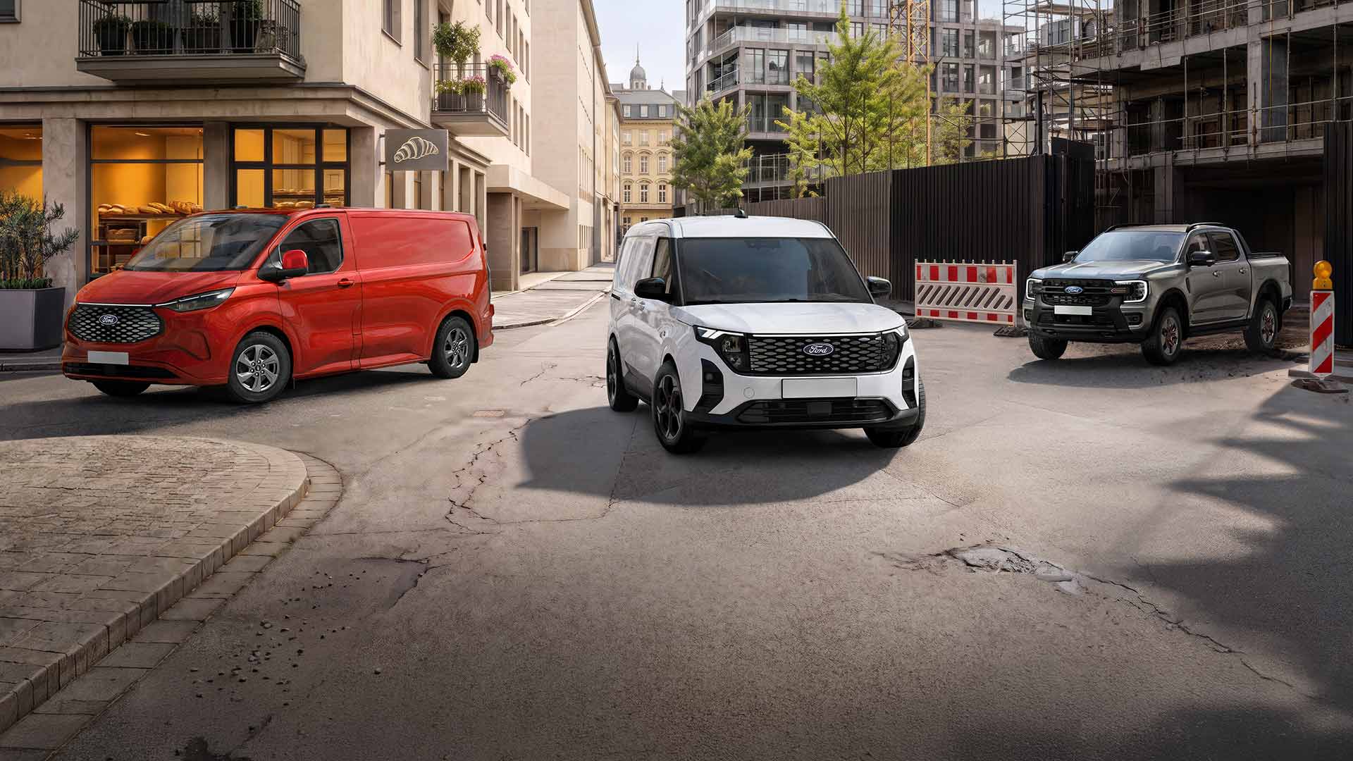 Drei Ford-Fahrzeuge, ein roter Transit Custom, ein weißer E-Transit Custom und ein grauer Ranger, stehen auf einer Stadtstraße. 