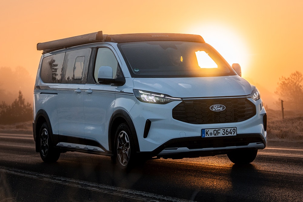Frontansicht der Ford Nugget Jubiläumsedition auf einer asphaltierten Strasse in einer nebligen Landschaft bei Sonnenaufgang.