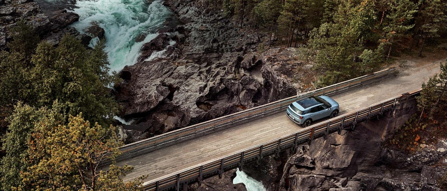 Der neue Ford Explorer in Hellblau in der Vogelperspektive fährt über eine schmale Holzbrücke über einen Fluss