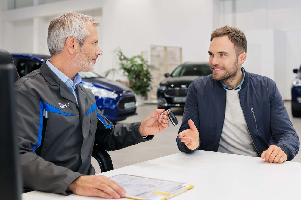 Zwei Männer sitzen sich in einem Autohaus gegenüber