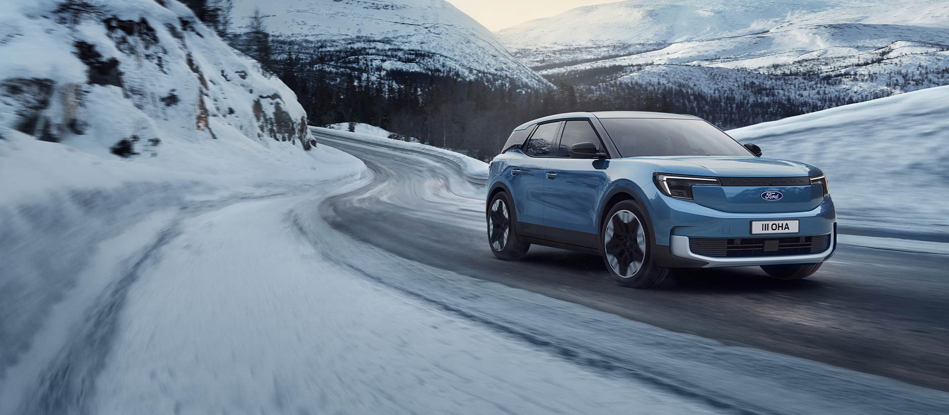 Blauer elektrischer Ford Explorer auf einer verschneiten Bergstrasse zur Darstellung der Leistung und Reichweite im Winter.