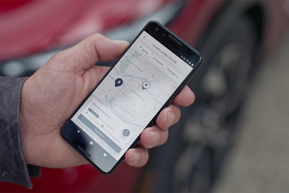 Ein Smartphone zeigt die FordPass™-App mit öffentlichen Ladestationen für Ford Elektrofahrzeuge in der Nähe an.