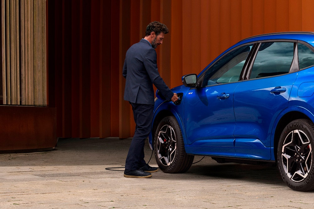 Eine Person schliesst ein Ford Plug-in-Hybrid-Fahrzeug an ein Ladegerät an.