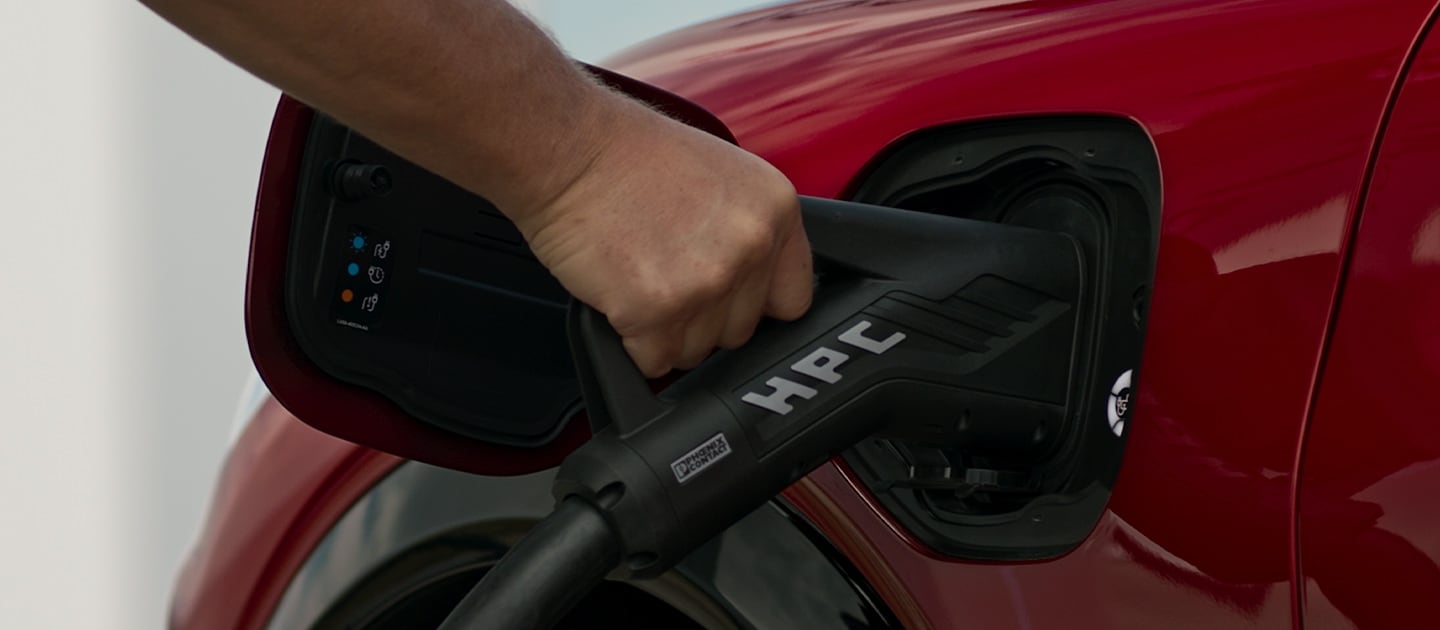 Nahaufnahme eines roten Ford Elektrofahrzeugs, das an eine öffentliche Ladestation zum Schnellladen angeschlossen ist.