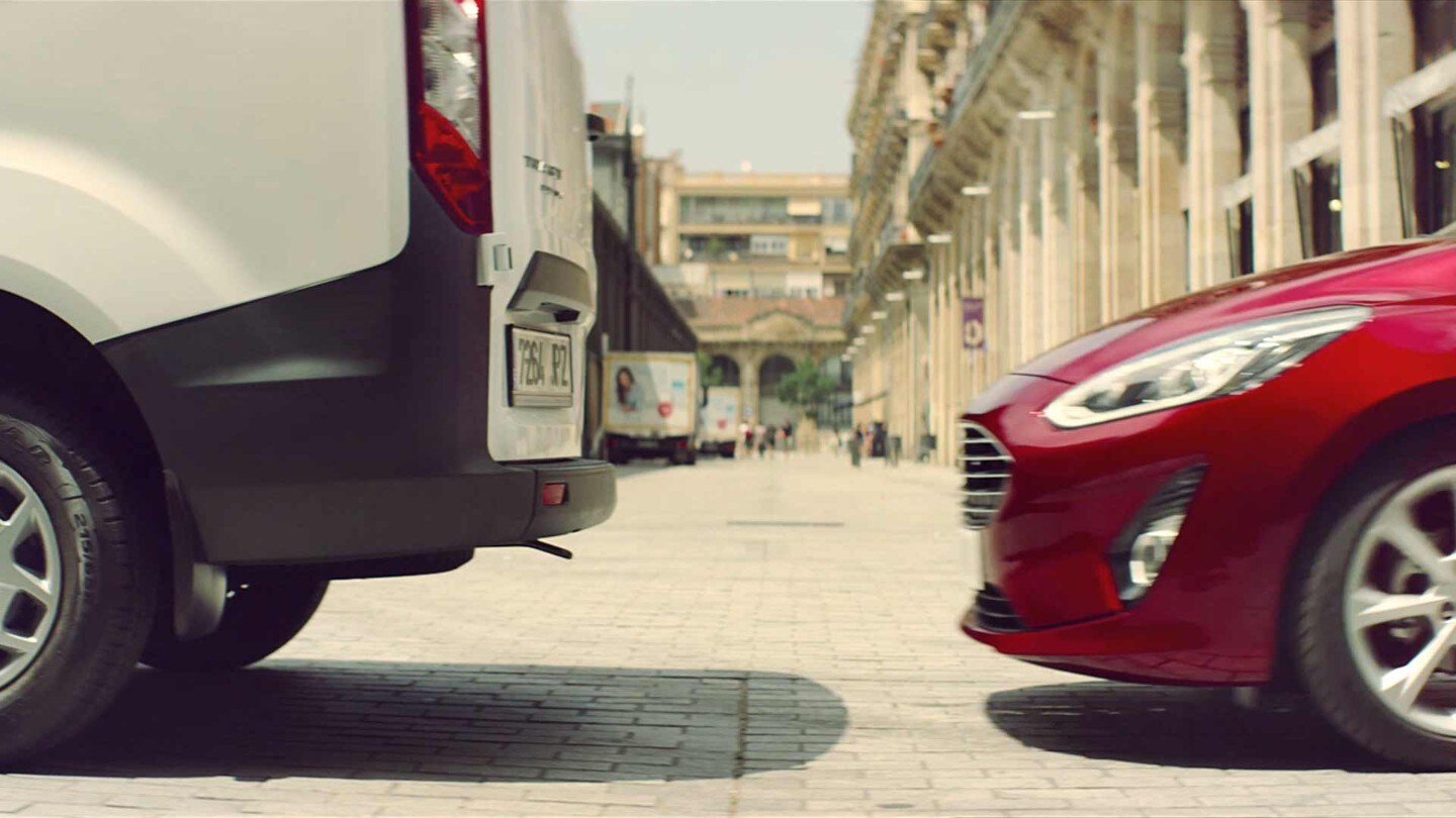 Ford Fiesta ST in Rot. Teilansicht der Front von der Seite hinter einem weissen Ford Transit. 