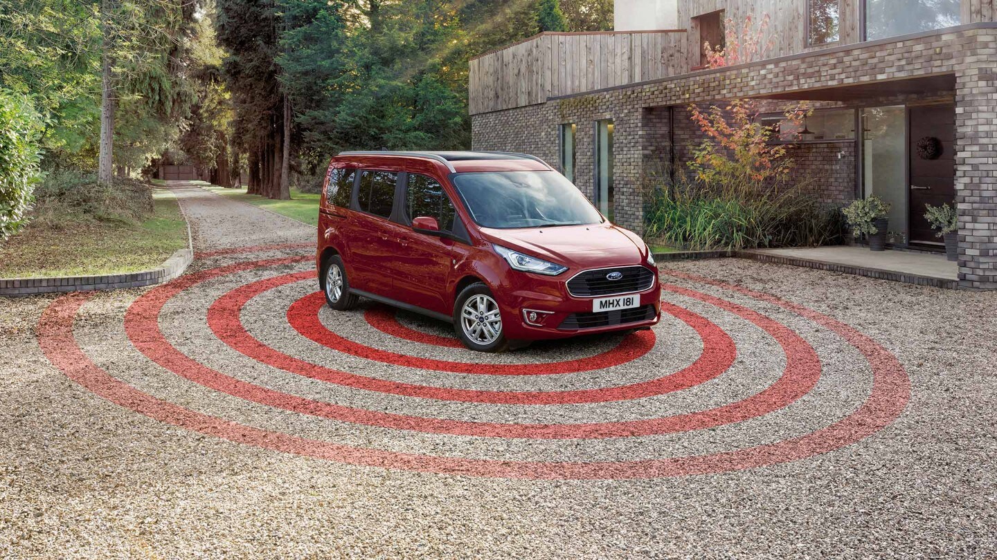 Ford Tourneo Connect in Rot ¾-Frontansicht parkt auf Kiesweg vor Wohnhaus mit Diebstahl-Alarmanlage Illustration