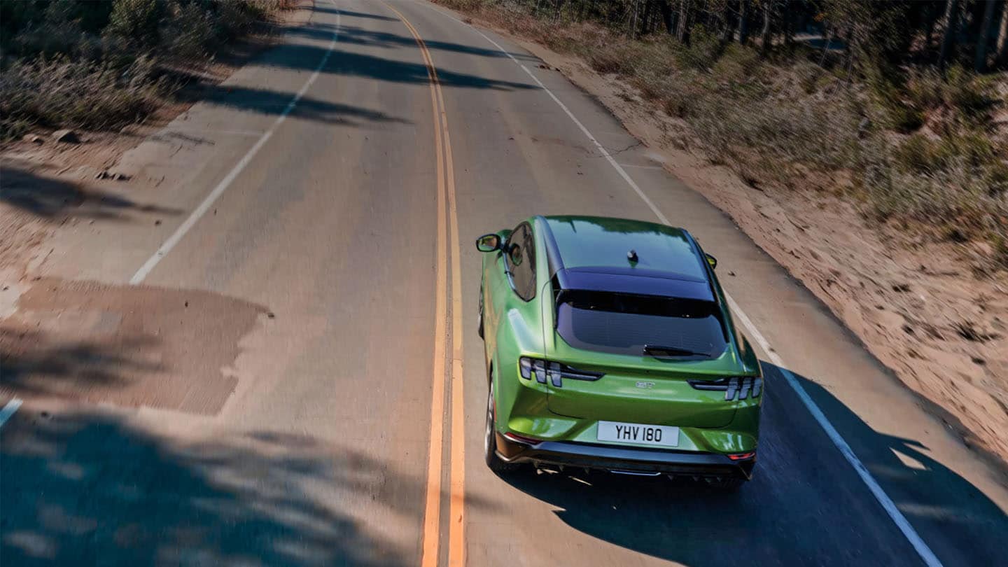 Ein grüner Ford Mustang Mach-E GT  fährt auf einer von Bäumen gesäumten Bergstrasse.