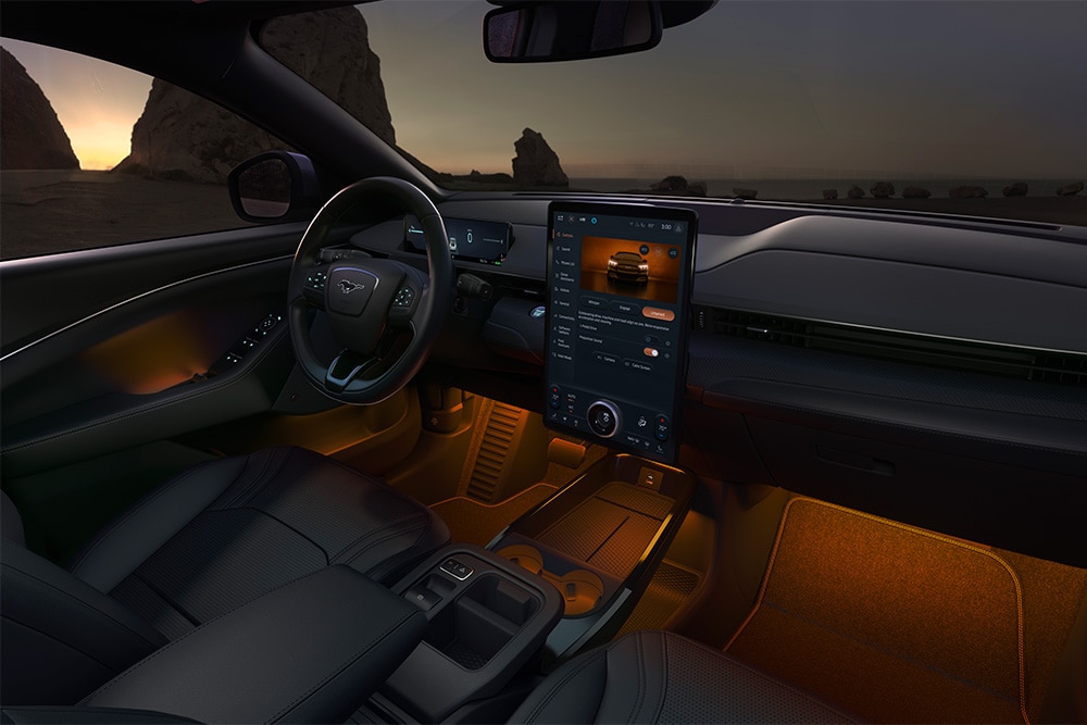 Ford Mustang Mach-E bei Nacht, mit dem 15,5-Zoll-SYNC-4-Touchscreen und auf Orange eingestellter LED-Ambientebeleuchtung.