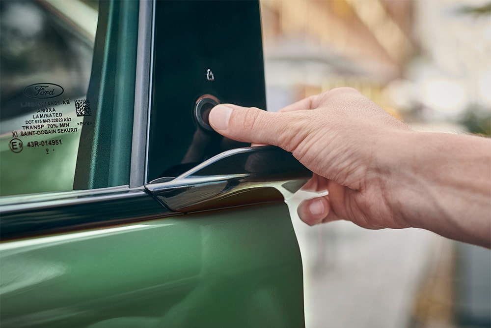 Hand, die durch Drücken eines Knopfes an der Tür eines grünen Ford Mustang Mach-E die Tür öffnet.