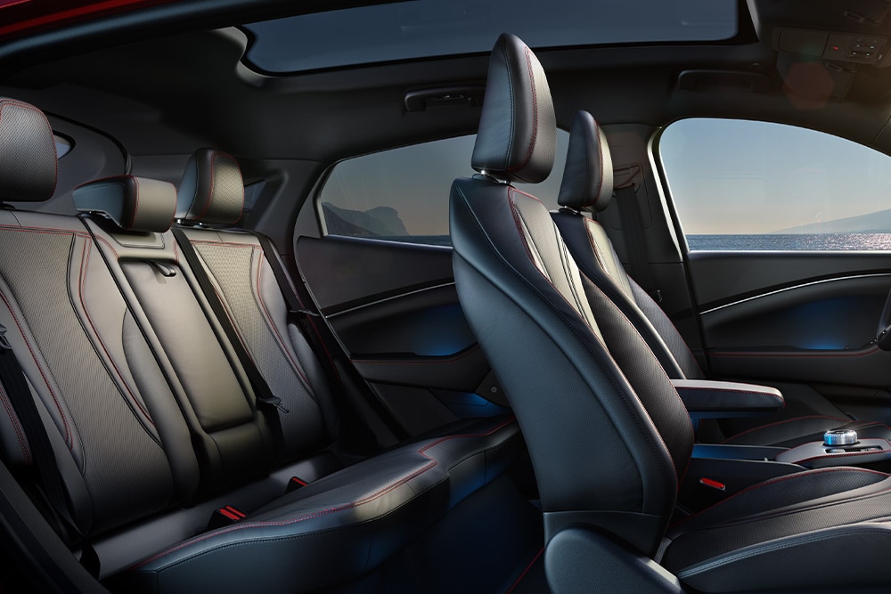 Das Interieur des Ford Mustang Mach-E mit fünf bequemen Sitzen mit schwarzem Material und roten Nähten.