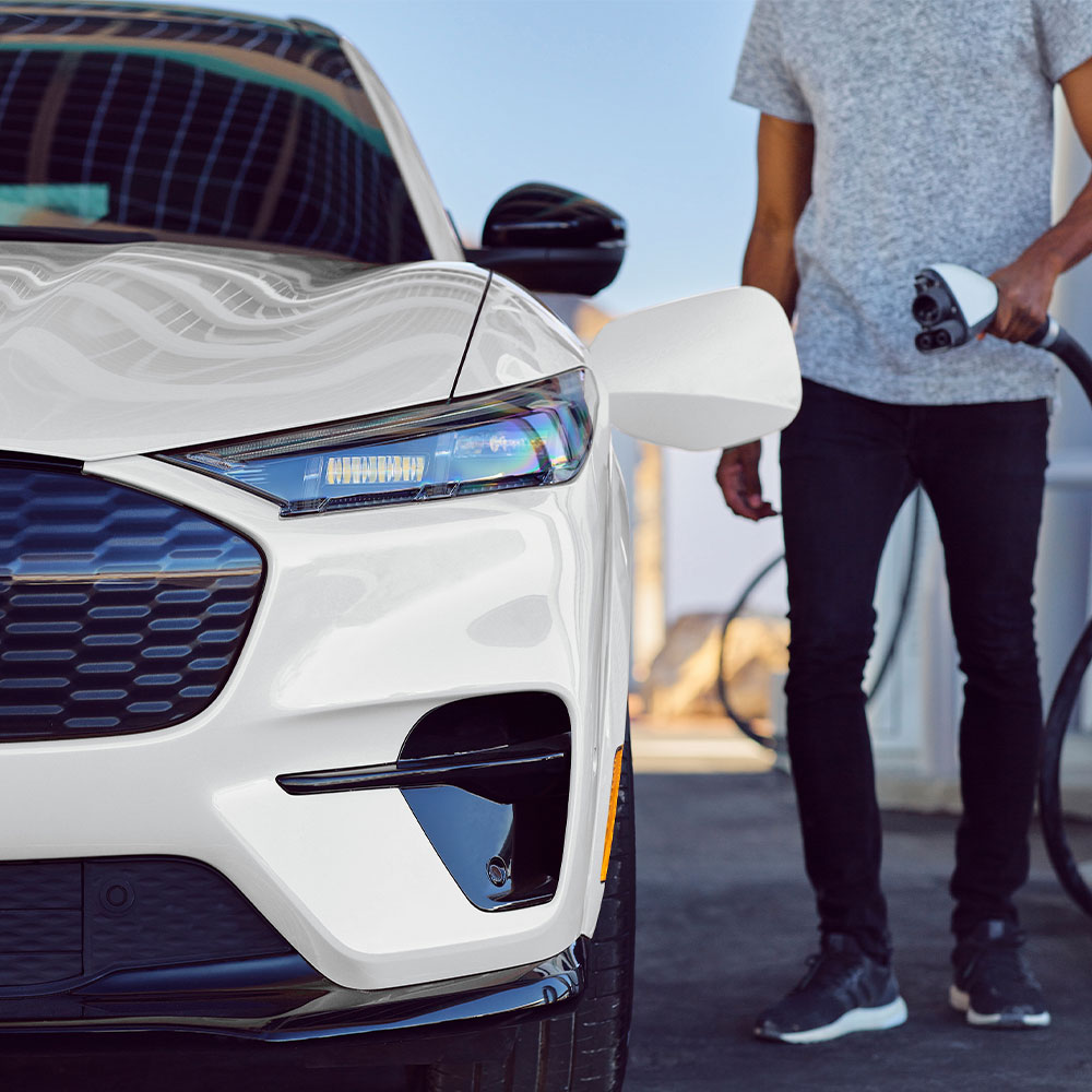 Person beim Laden eines weissen Ford Mustang Mach-E mit einem EV-Ladekabel.