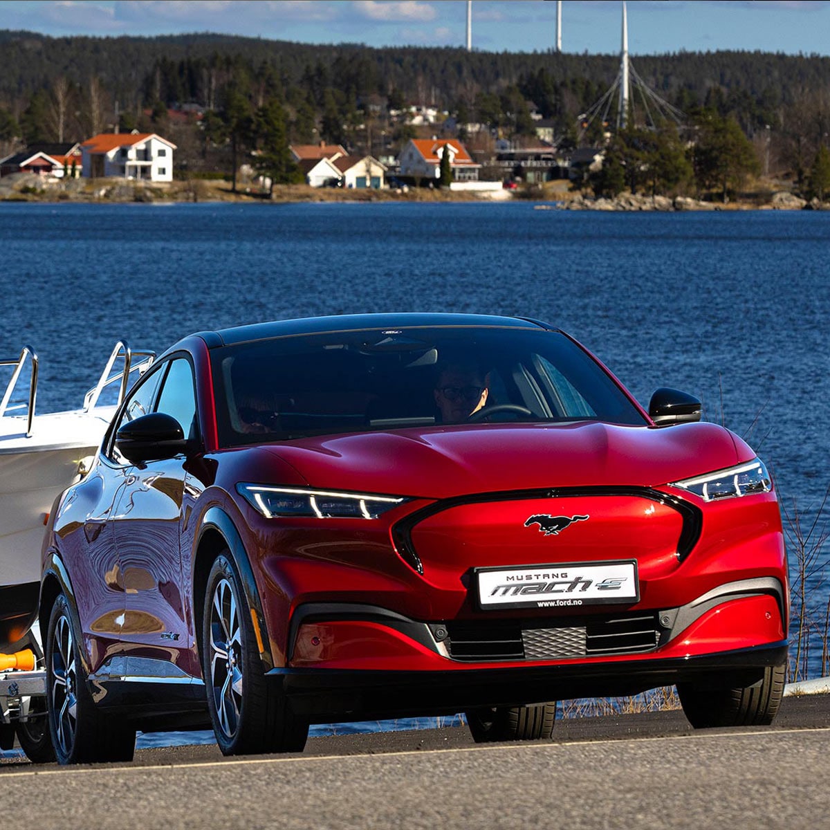 Ford Mustang Mach-E in Rot Frontansicht wie er ein Boot auf einem Anhänger an einem See zieht