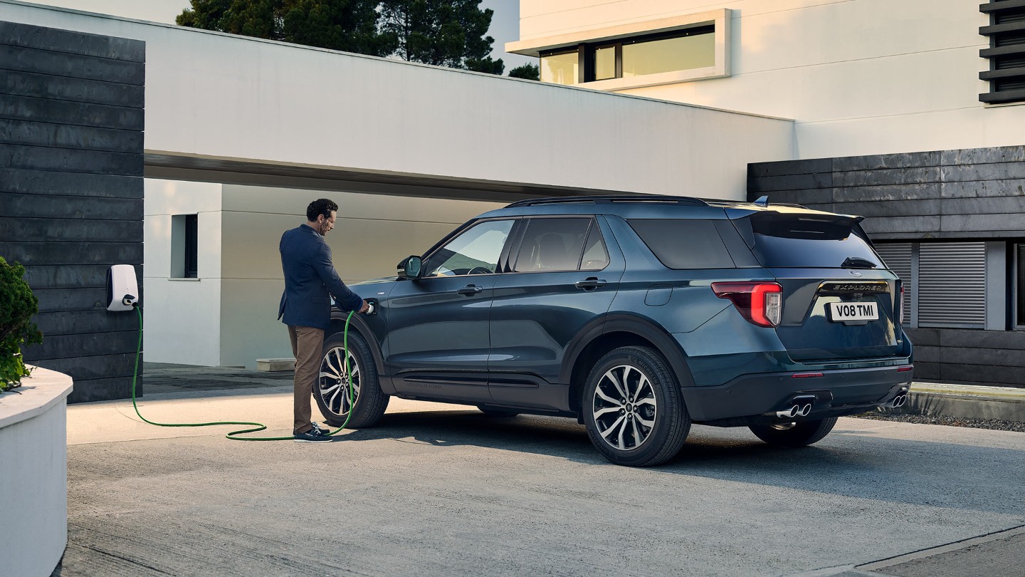 Ford Explorer Plug-in-Hybrid in Blau. ¾-Heckansicht. Ladevorgang vor einem Gebäude.