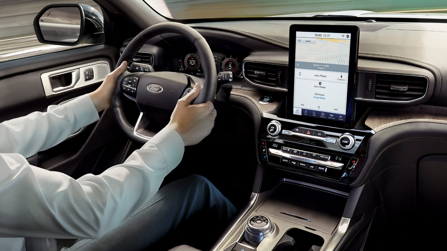 Ford Explorer Plug-In Hybrid. Innenraum. Detailansicht Lenkrad und Mittelkonsole mit Touchscreen. Hände des Fahrers am Lenkrad