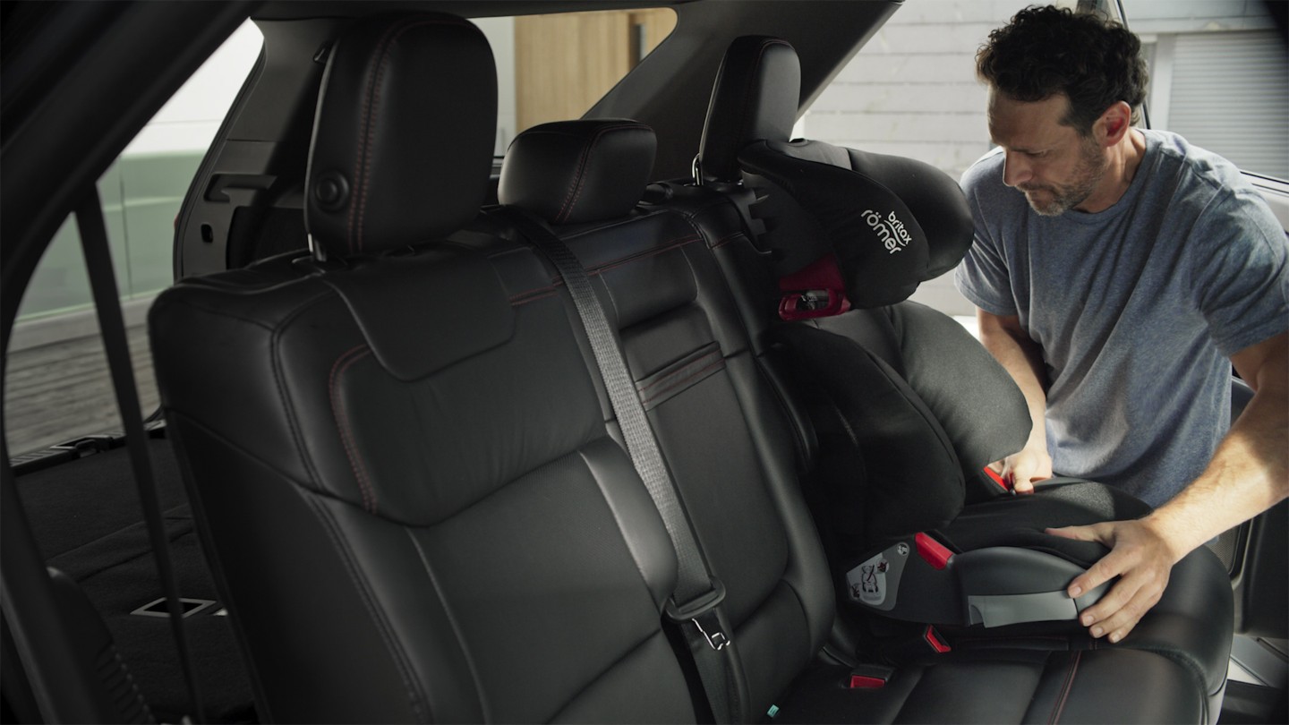 Ford Explorer Plug-In Hybrid. Innenraum Detailansicht. Mann befestigt Kindersitz auf äusserem Rücksitz