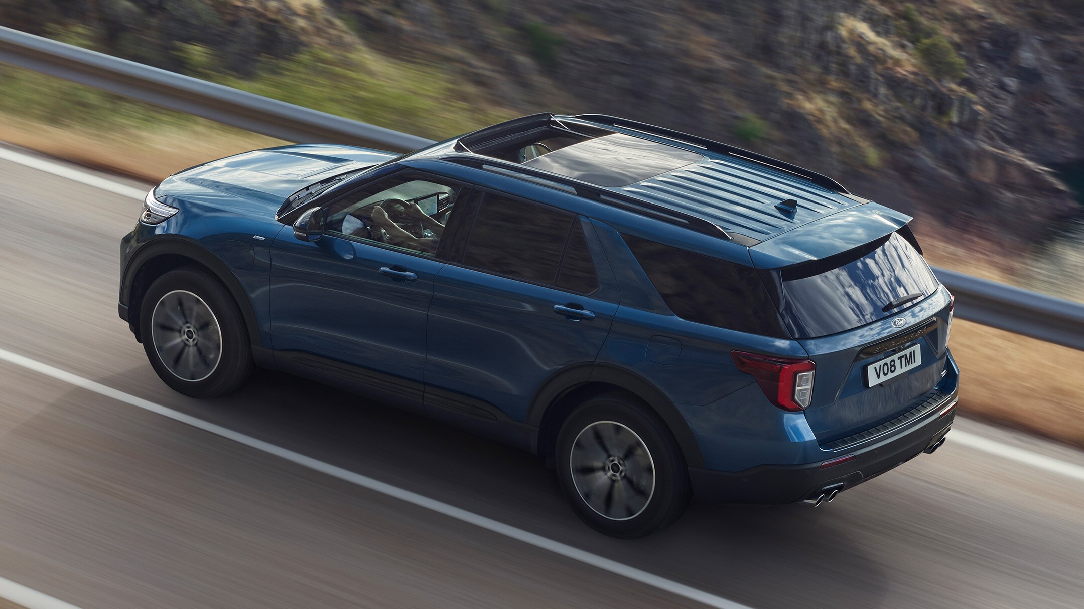 Ford Explorer in Blau. Dreiviertel-Heckansicht. Eine Strasse in den Bergen bergauf fahrend