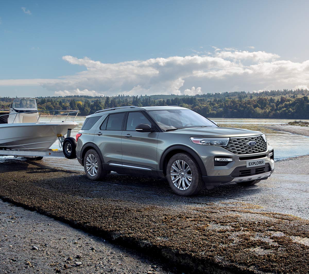 Ford Explorer Plug-In Hybrid in Silber. Dreiviertel-Frontansicht. Mit Bootsanhänger an einem See