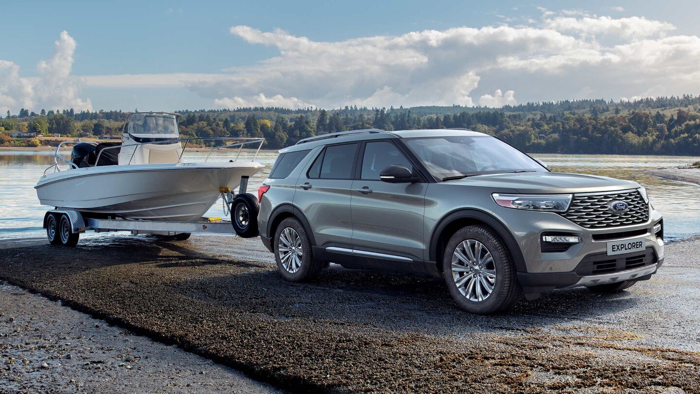 Ford Explorer Plug-In Hybrid in Silber. Dreiviertel-Frontansicht. Mit Bootsanhänger an einem See