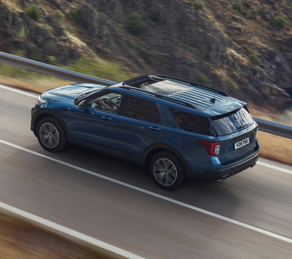 Ford Explorer Plug-In Hybrid in Blau. Dreiviertel-Heckansicht. Eine Strasse in den Bergen bergauf fahrend