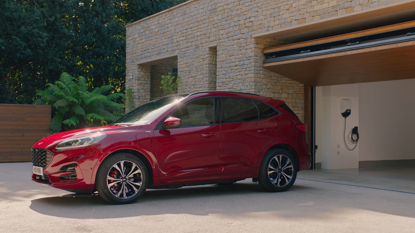 Ford Kuga Plug-in-Hybrid (PHEV) in Rot. Seitenansicht, vor einer geöffneten Garage mit Wallbox stehend