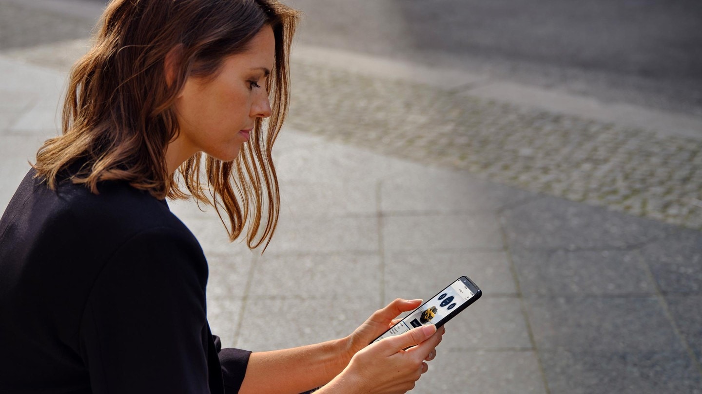 Frau am Strassenrand sitzend und auf ihr Smartphone blickend