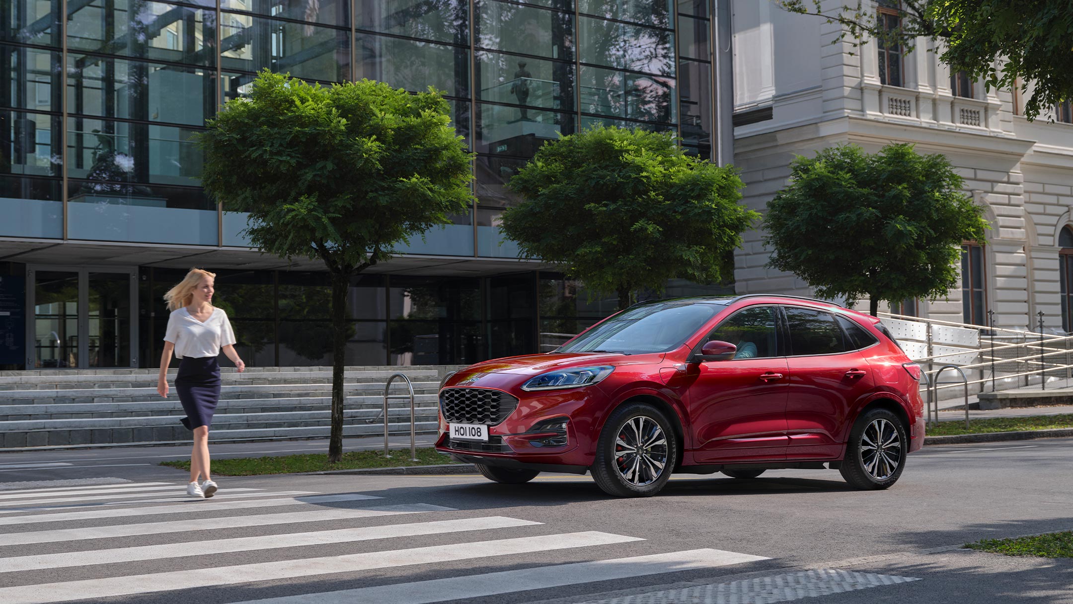 Ford Kuga in Rot. Seitenansicht, vor einem Zebrastreifen in der Stadt stehend