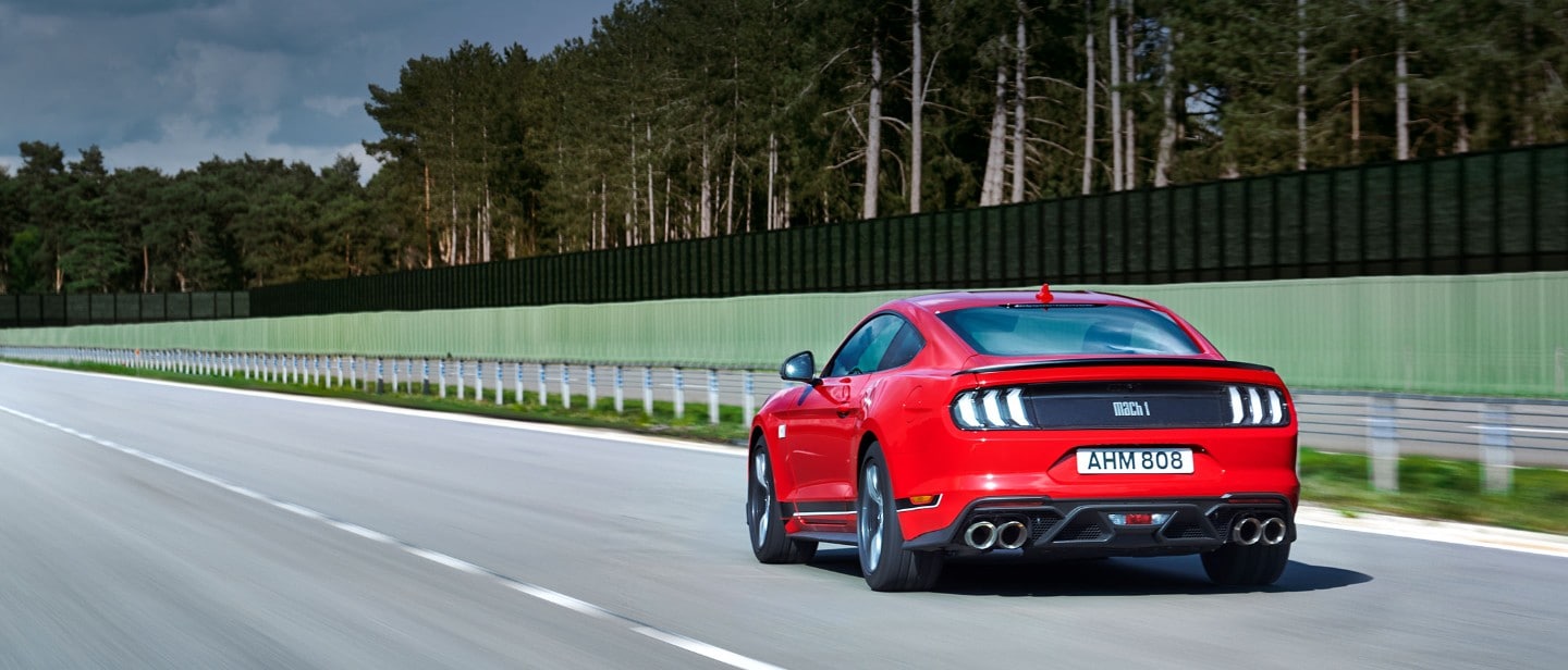 Ford Mustang Mach 1 in Rot. Dreiviertel-Heckansicht, auf einer Strecke fahrend