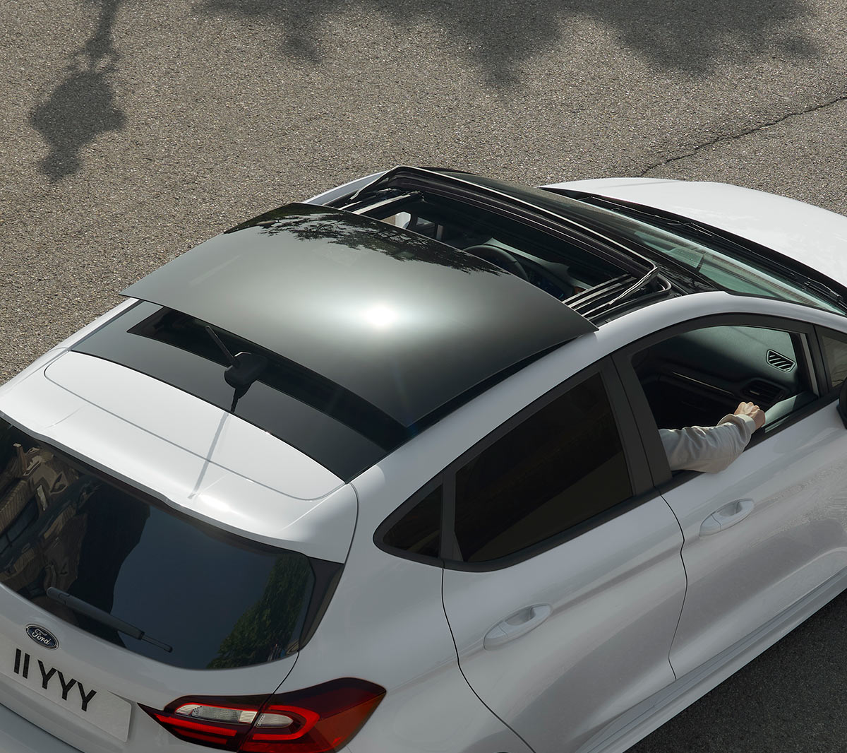 Ford Fiesta in Weiss. Dreiviertel-Heckansicht von oben mit Blick auf das Panorama-Schiebedach, auf einer Strasse fahrend.