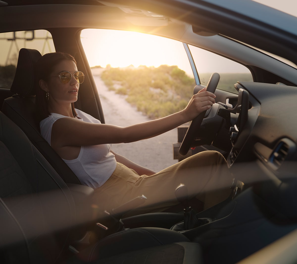 Ford Fiesta. Innenraumansicht. Eine Frau sitz bei geöffneter Fahrertür auf dem Fahrersitz. Im Hintergrund ein Sonnenuntergang.