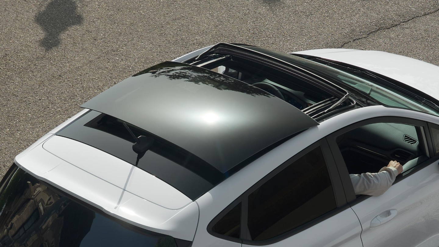 Ford Fiesta in Weiss. Dreiviertel-Heckansicht von oben mit Blick auf das Panorama-Schiebedach, auf einer Straße fahrend.