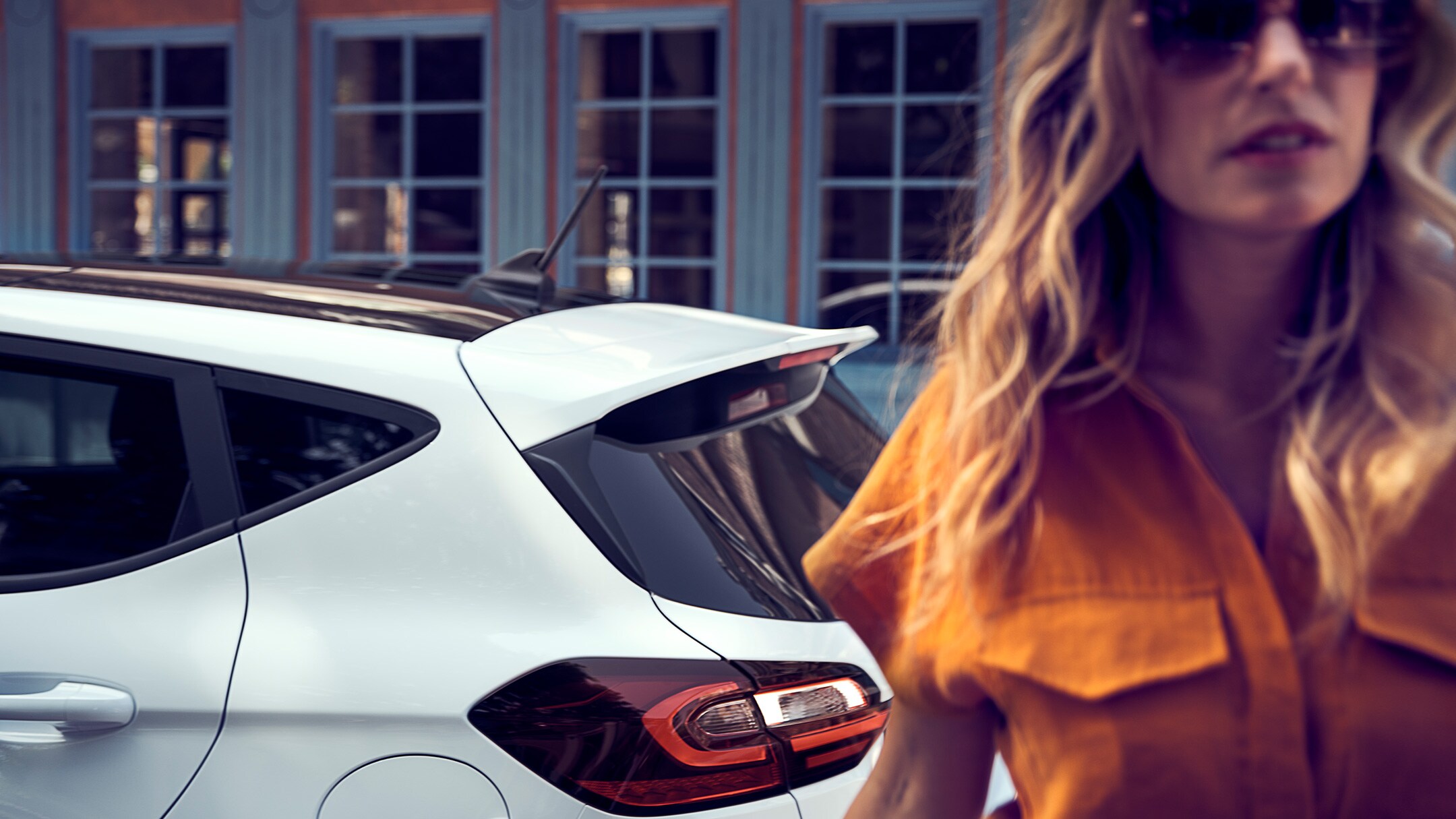 Ford Fiesta in Weiss. Seitenansicht des Hecks, vor einem Haus parkend mit Frau im Vordergrund.