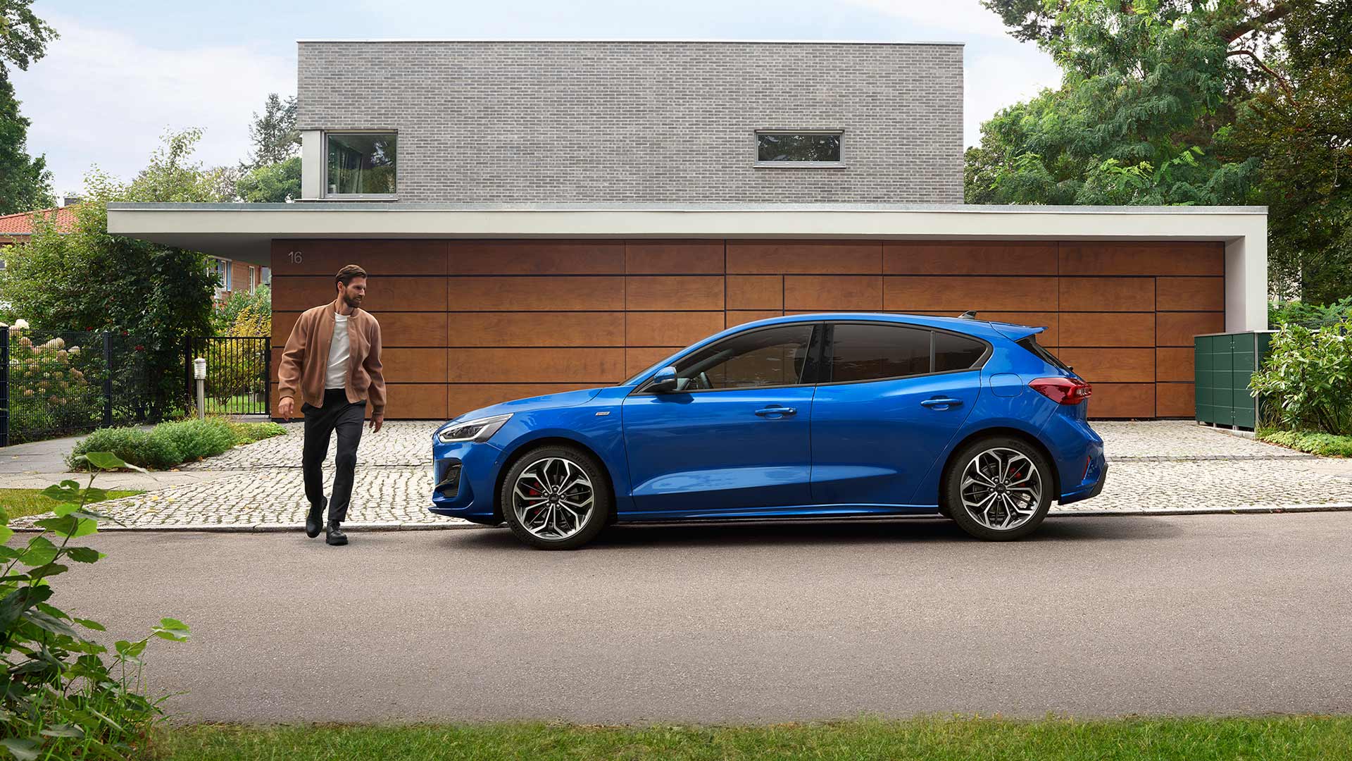 Ein Mann nähert sich einem blauen Ford Focus, der vor einem Haus geparkt ist.