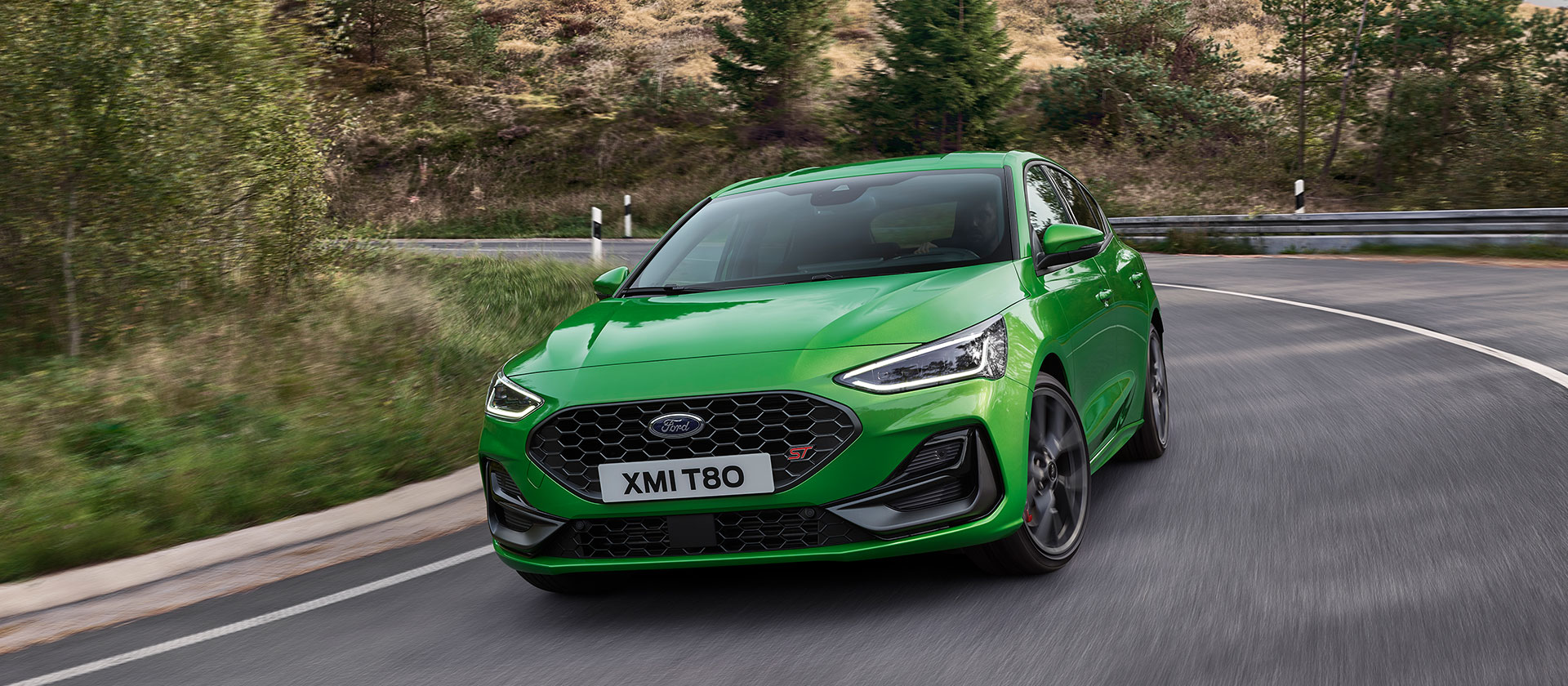 Ein Ford Focus ST in Mean Green fährt auf einer malerischen Strasse um eine Kurve.