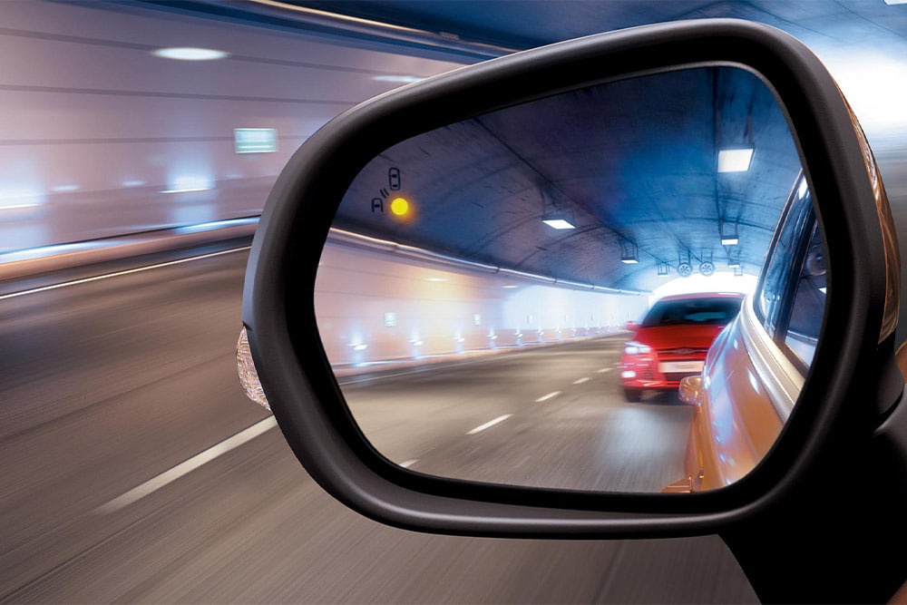 Ein Seitenspiegel in einem Tunnel aus der Perspektive der fahrenden Person: Ein rotes Auto nähert sich im toten Winkel.
