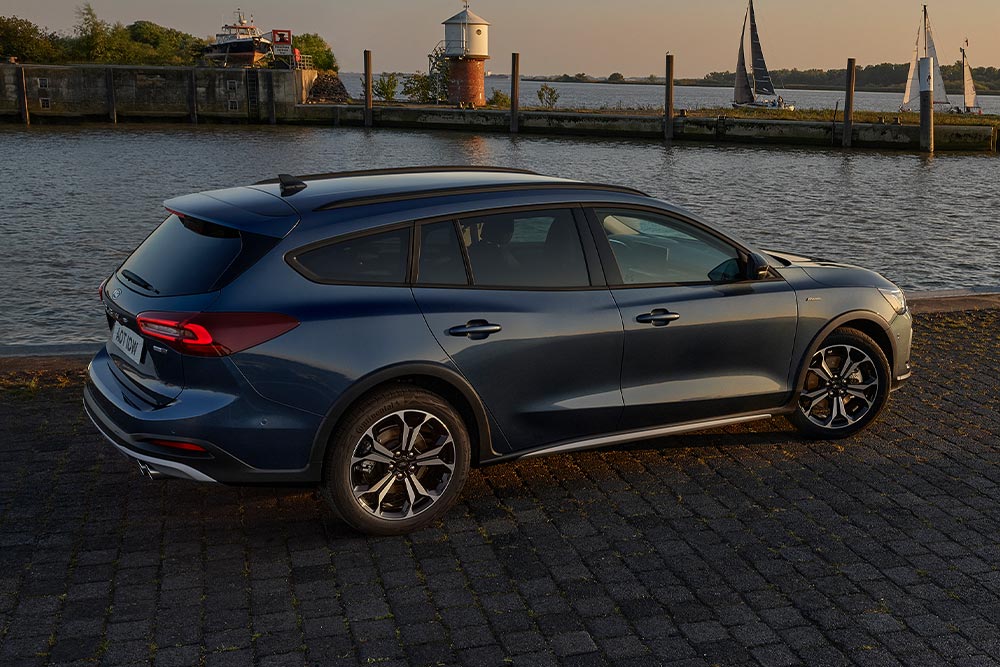Ein dunkelblauer Ford Focus Active Turnier, geparkt neben einem Gewässer in der Abenddämmerung.