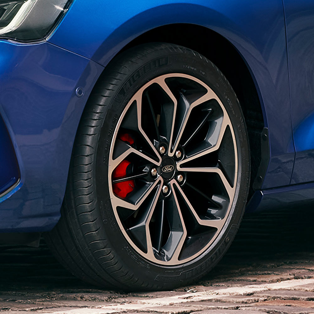 Nahaufnahme der grauen Leichtmetallfelgen mit roten Bremssätteln an einem blauen Ford Focus.