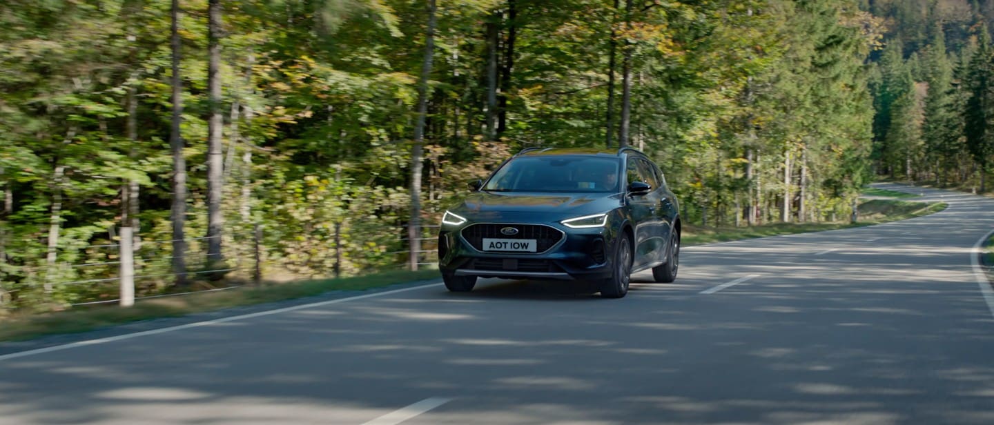 Ford Focus in Blau. Dreiviertel-Heckansicht, in der Natur fahrend mit Bäumen im Hintergrund.