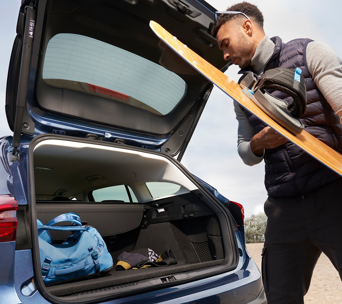 Ford Focus Active in Blau. Dreiviertel-Heckansicht, ein Mann verstaut ein Snowboard im Kofferraum.