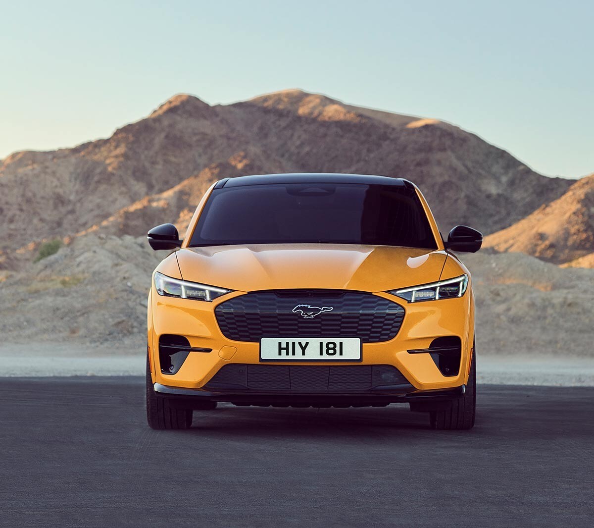 Ford Mustang Mach-E GT in Orange. Frontansicht, auf einem Parkplatz vor bergen parkend