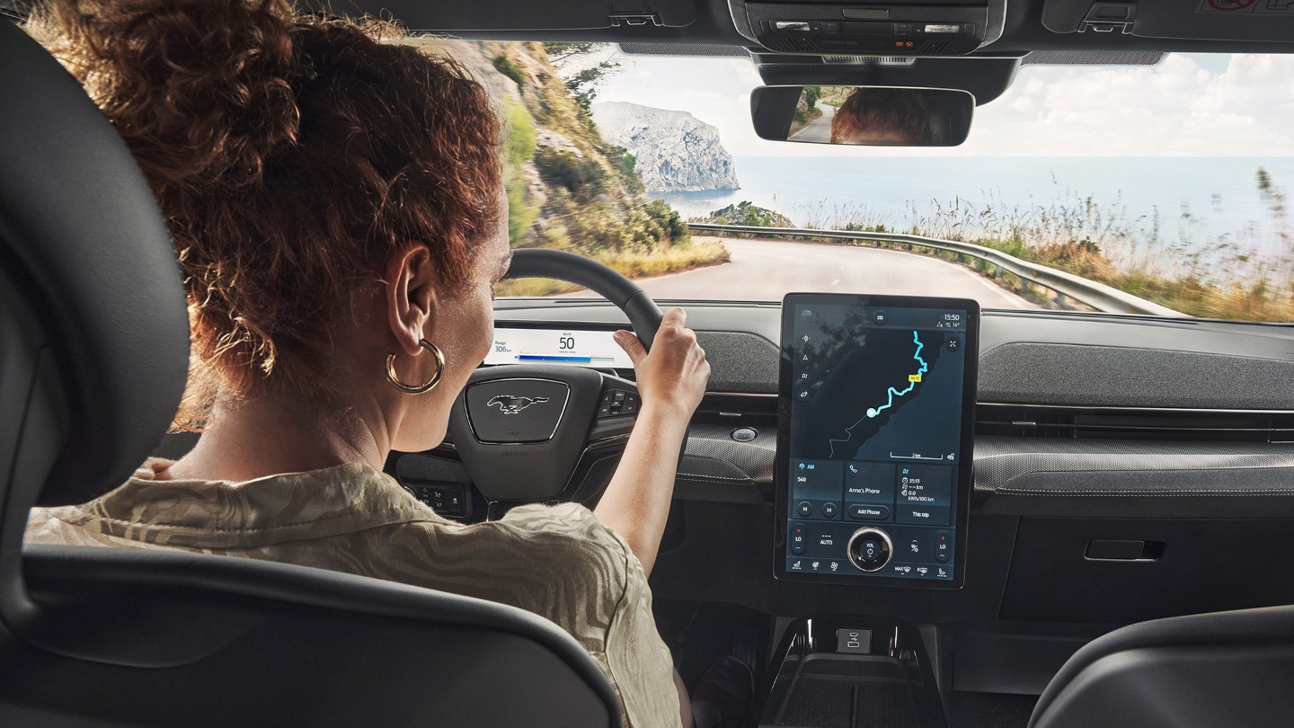 Ford Mustang Mach-E GT. Innenraumansicht, eine Frau betrachtet den Ford SYNC 4 Touchscreen.