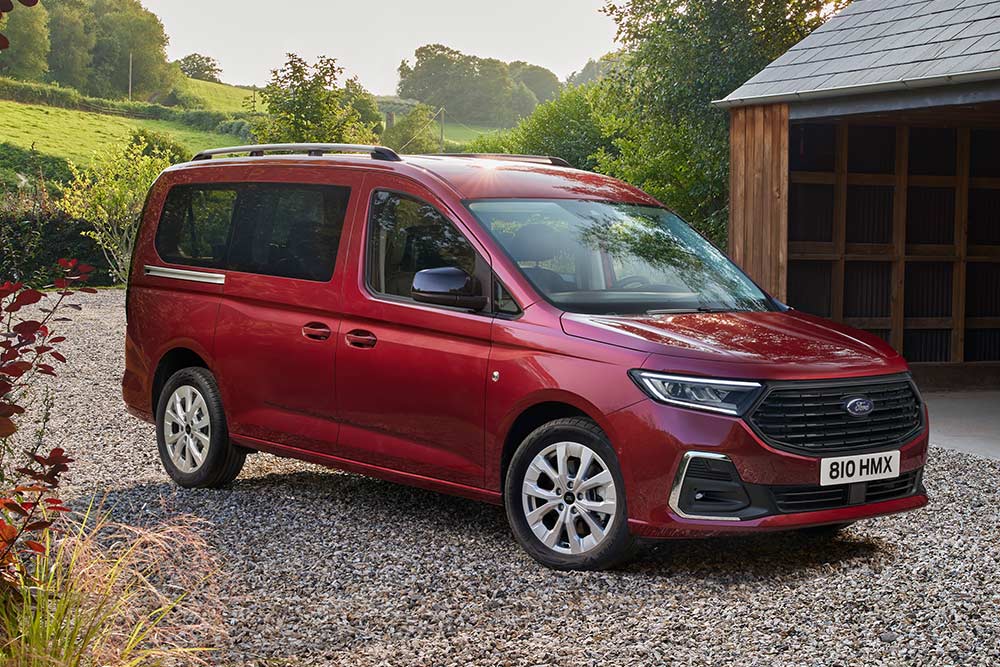 Ford Grand Tourneo Connect in Rot ¾-Frontansicht parkt auf Kiesweg vor Wohnhaus 
