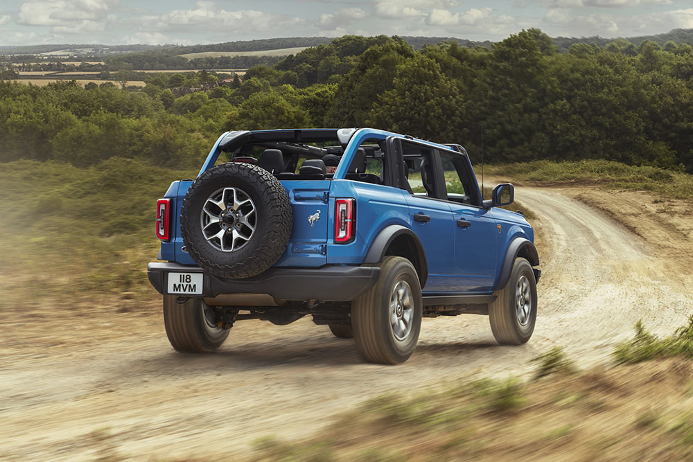 Eine Rückansicht eines blauen Ford Bronco, der durch eine ländliche Landschaft fährt.