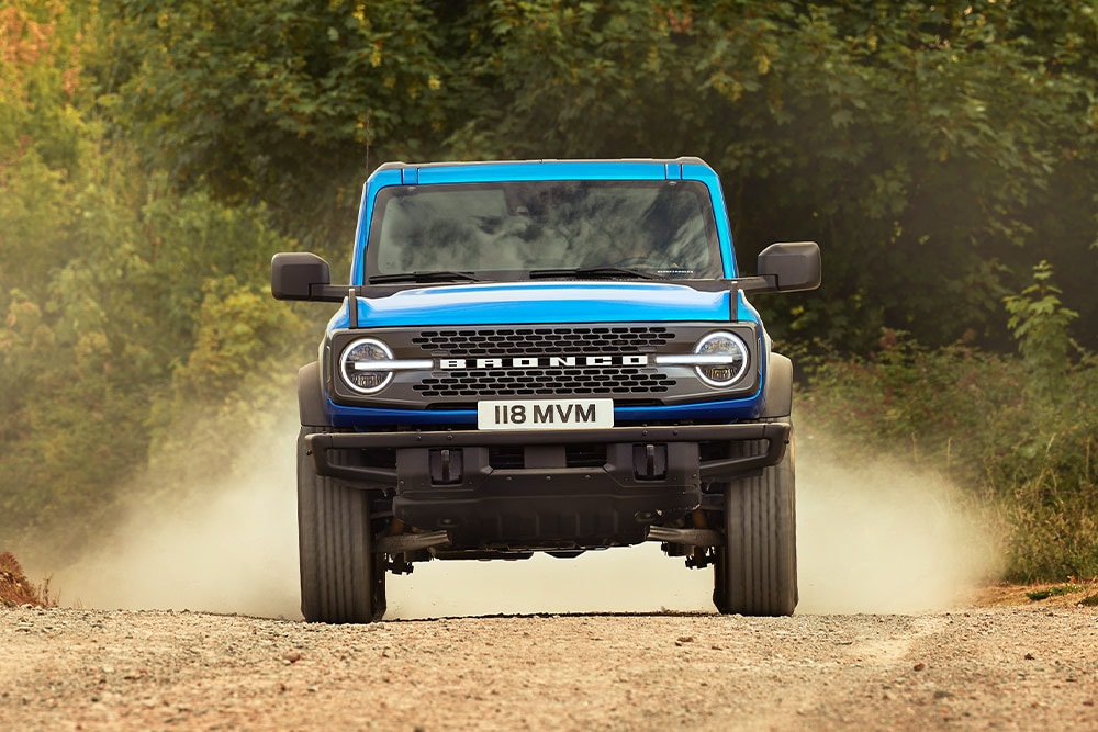 Vorderansicht eines blauen Ford Bronco, der auf einer unbefestigten Strasse fährt.