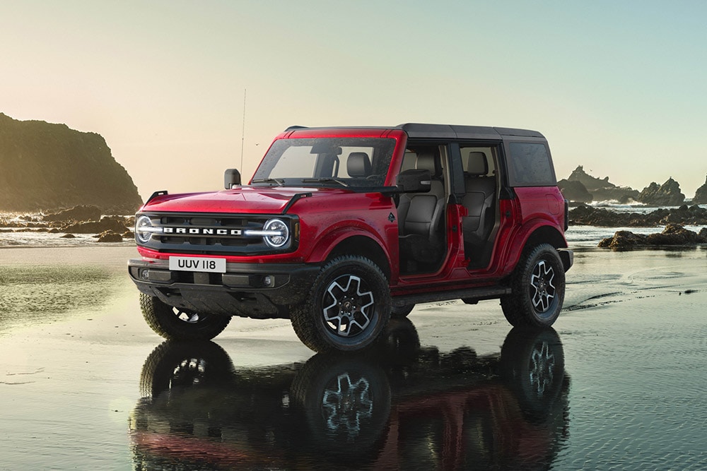Seitenansicht eines roten Ford Bronco mit entfernten Türen, der an einem nassen Sandstrand geparkt ist.